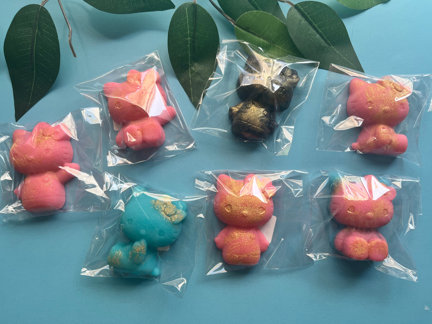 Colorful Hello Kitty candies in clear packaging on a blue surface with green leaves.