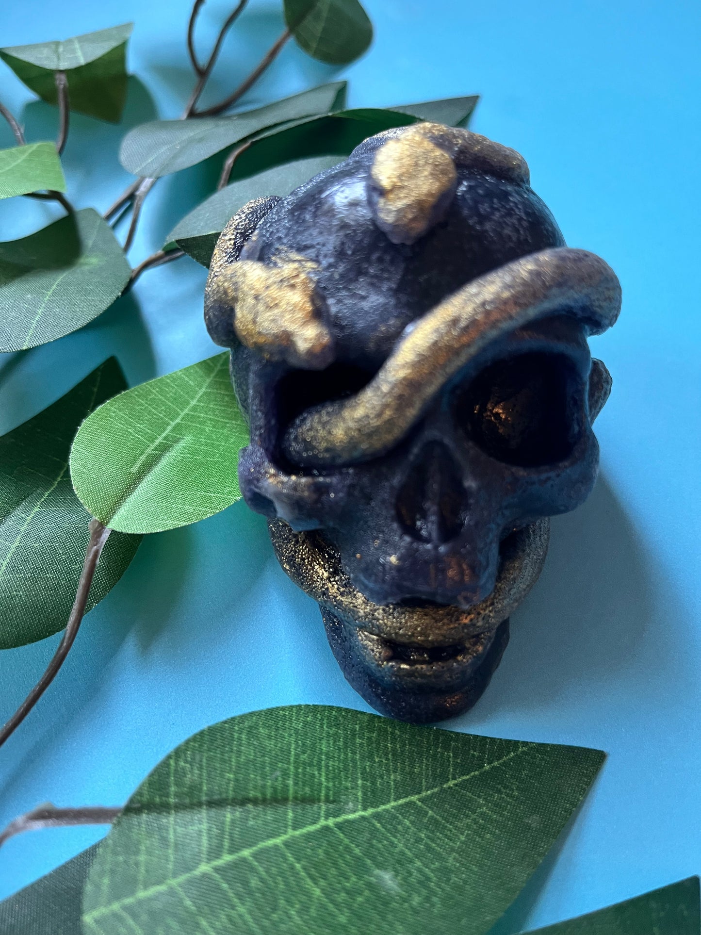 Crystal Candy skull with gold accents on a blue background with green leaves