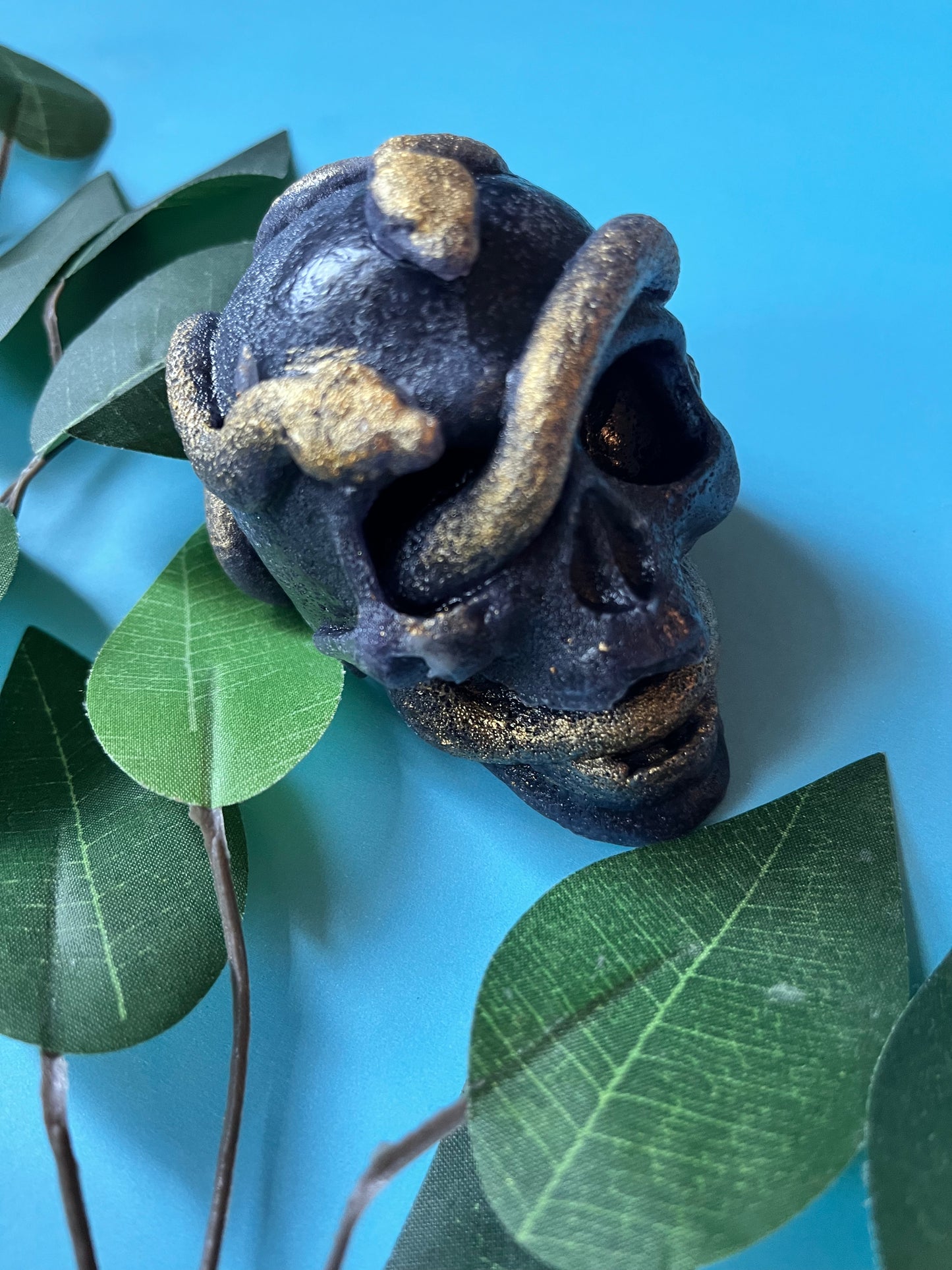 Decorative skull with gold accents on a blue background with green leaves