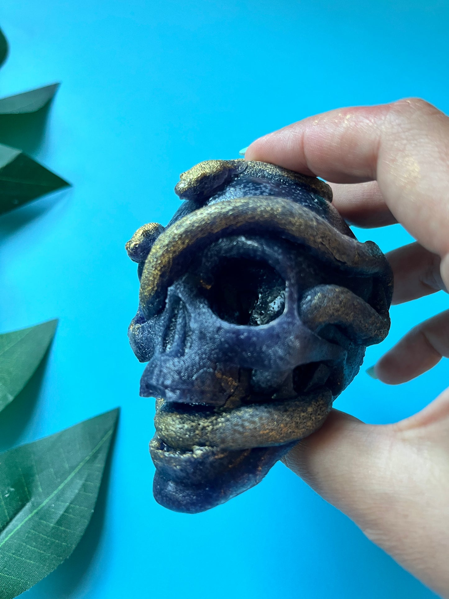 Hand holding a decorative skull figurine with gold accents against a blue background