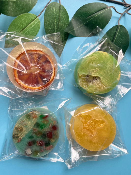 Four extra-large crystal candies on a blue background, each wrapped in clear plastic with visible fruit centers — kiwi, orange, pineapple, and mixed fruit.