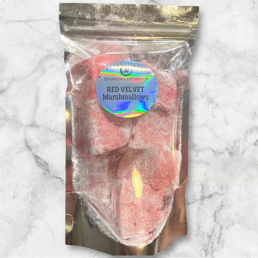 Resealable pouch of red velvet marshmallows, dusted and glowing in a holographic Diamond Delights label, placed on a marble background.