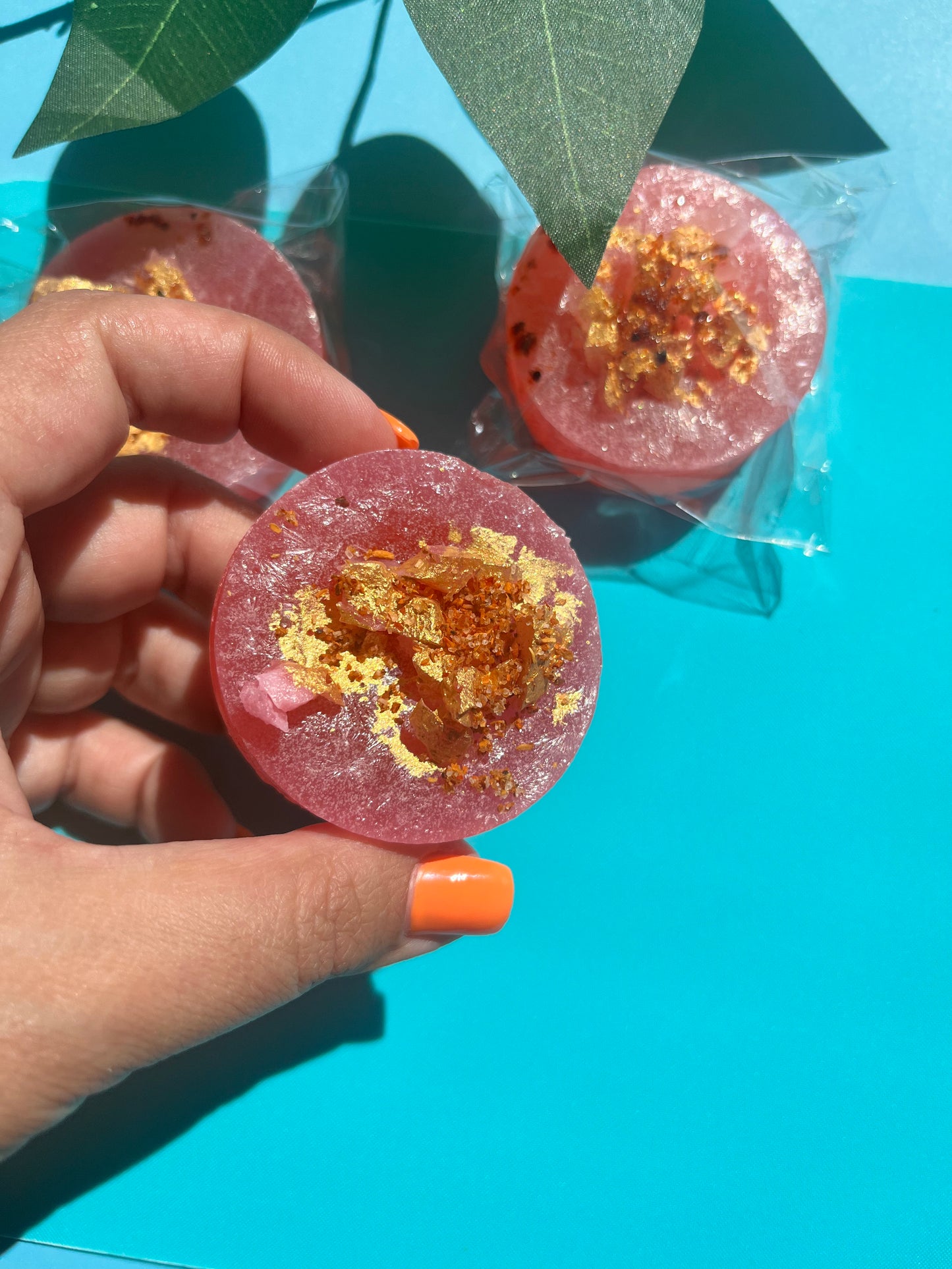 Pink candy with gold flakes held by a hand against a blue background