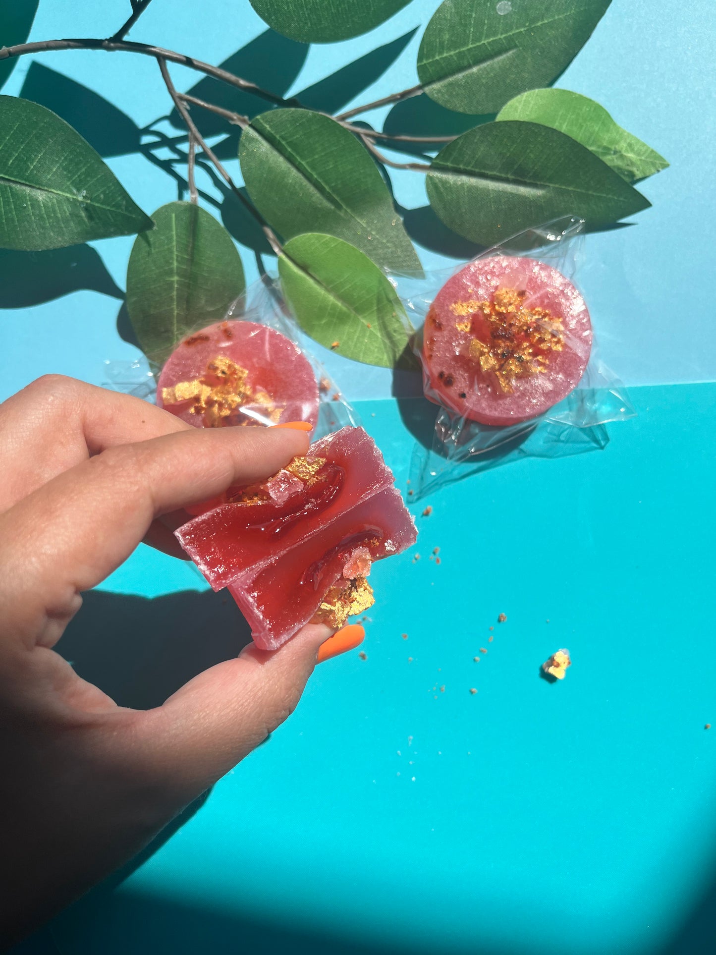 Hand holding a red jelly-like dessert with gold sprinkles against a blue background with green leaves.