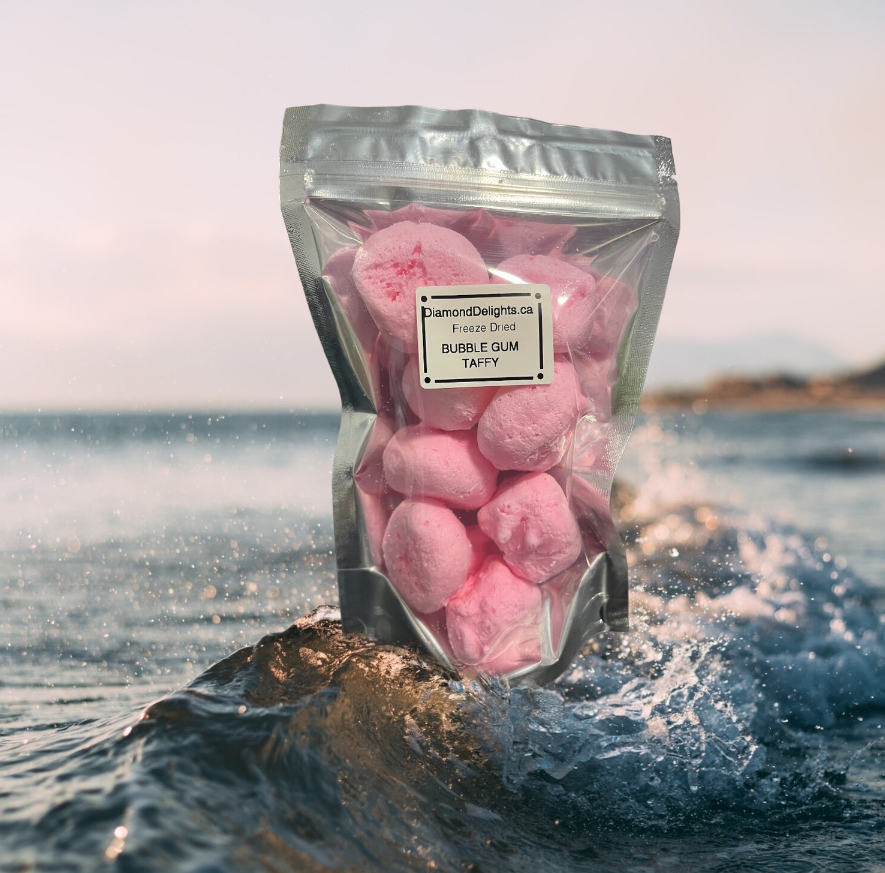 Bag of pink freeze-dried bubble gum salt water taffy pieces, styled on ocean rocks under soft natural light.