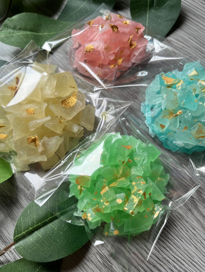 Colorful crystal candy gem clusters in clear wrappers by Diamond Delights, displayed on green leaves