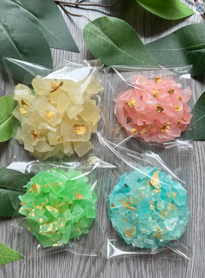 Blue, pink, yellow and green crystal candy gem clusters in clear wrappers by Diamond Delights, displayed on green leaves
