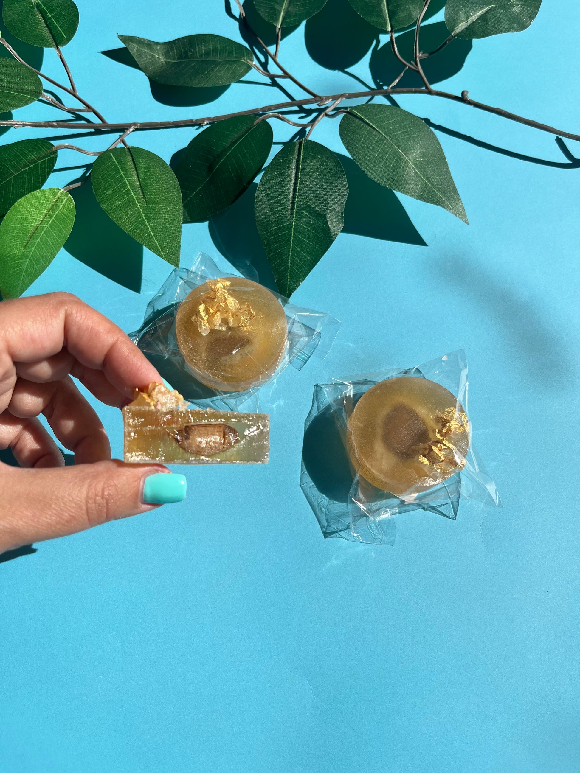 Hand holding tiramisu crystal candy with coffee shell and creamy center, topped with edible gold flakes