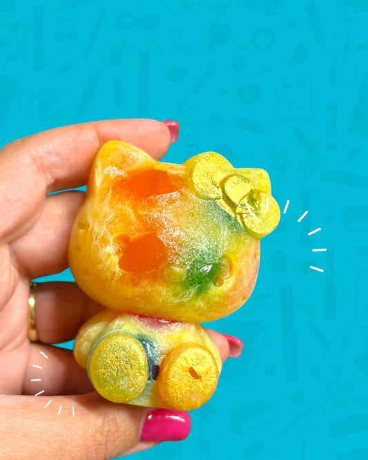 Colorful jelly candy shaped like a cat held by a hand against a blue background