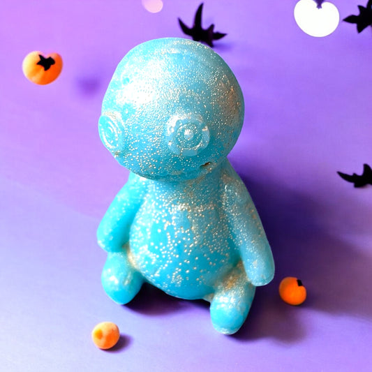 Blue glittery figurine on a purple background with small orange and black objects.