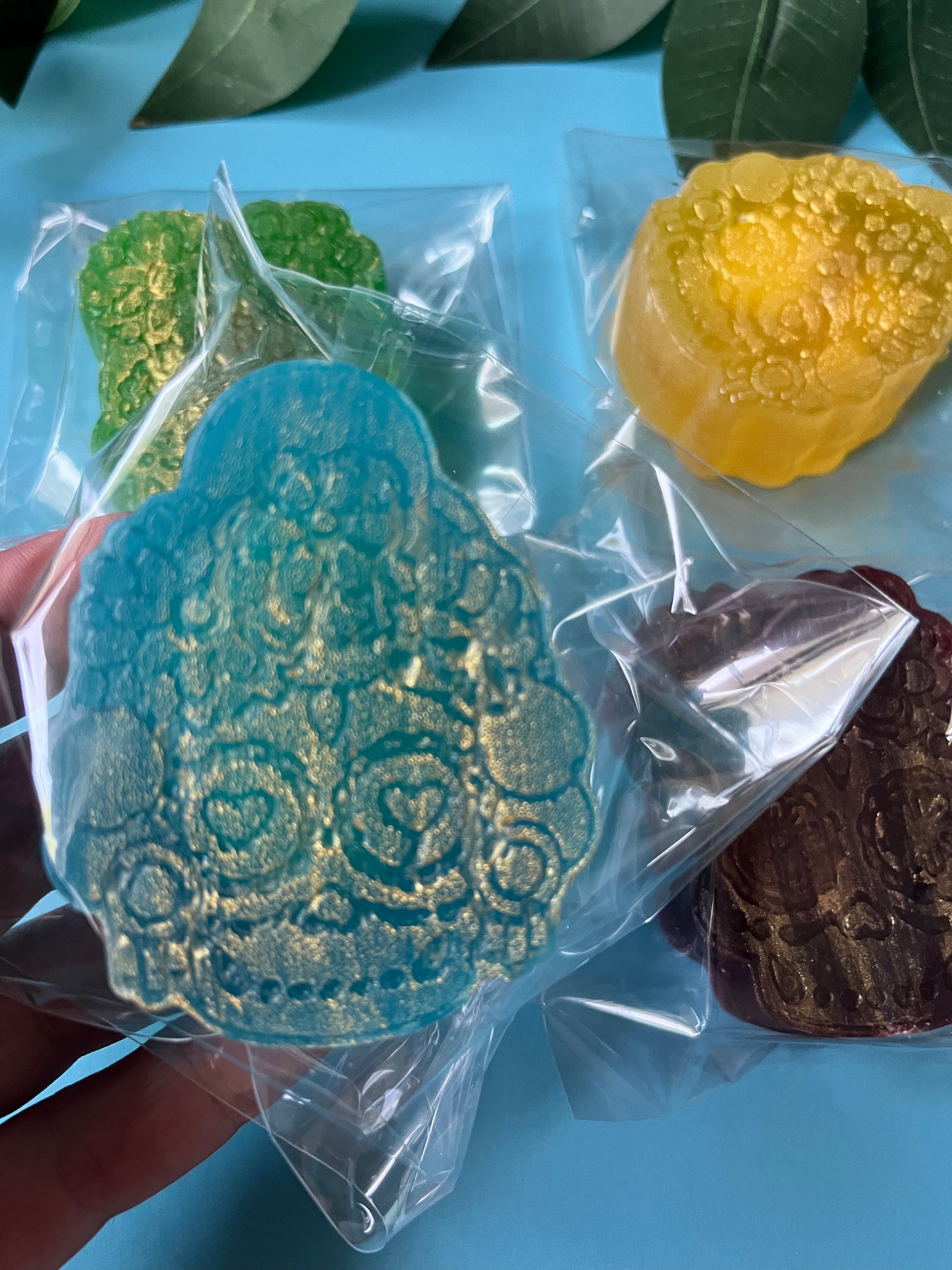 Delicious crystal candy in clear packaging on a blue surface with green leaves.