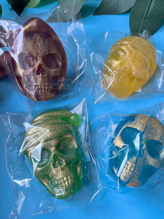Four skull-shaped Crystal Candies in different colors (brown, yellow, green, blue) on a blue surface with leaves.
