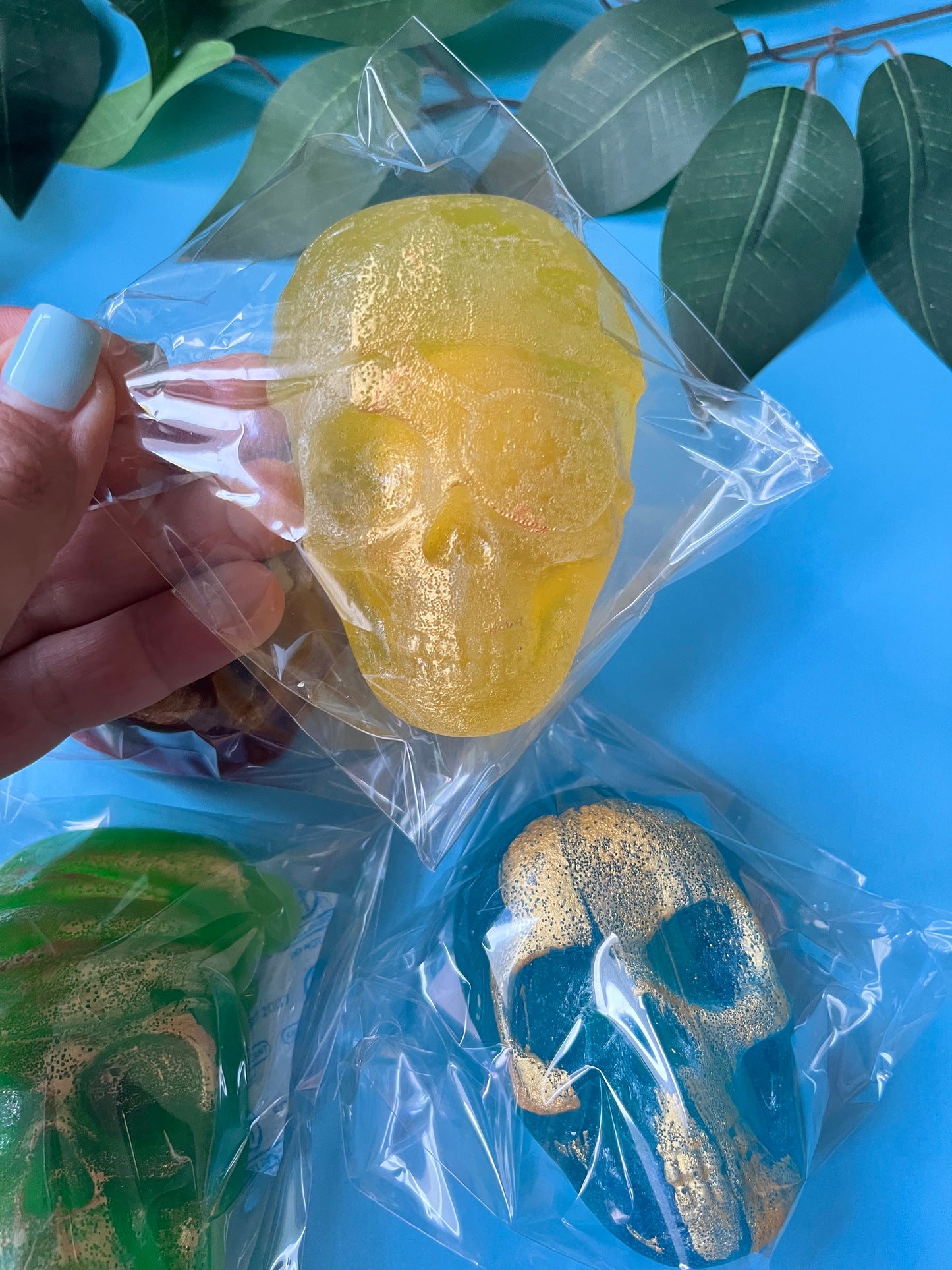 Gold skull-shaped Crystal Candy in clear packaging on a blue surface with green leaves.