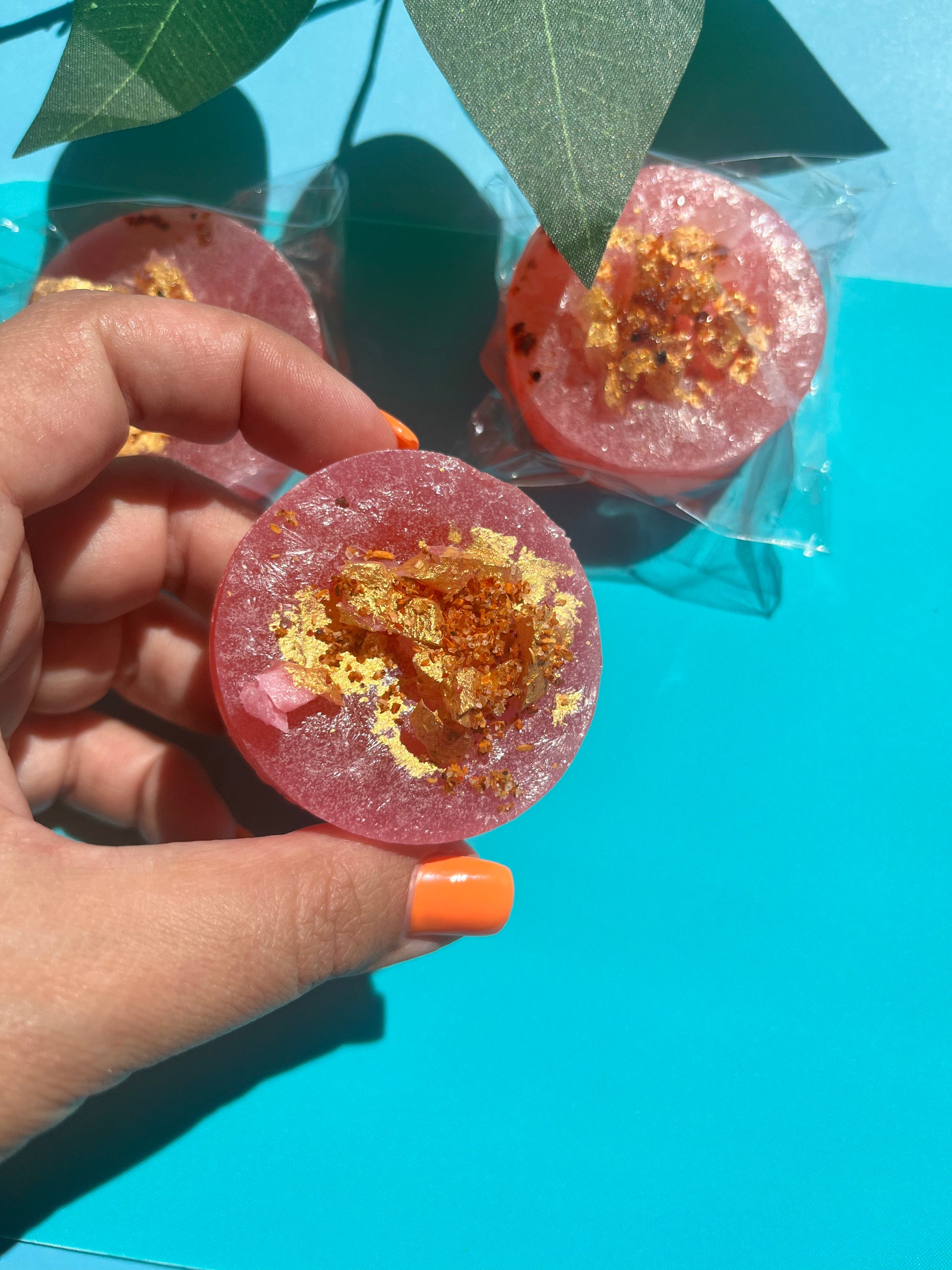 Pink candy with gold flakes held by a hand against a blue background