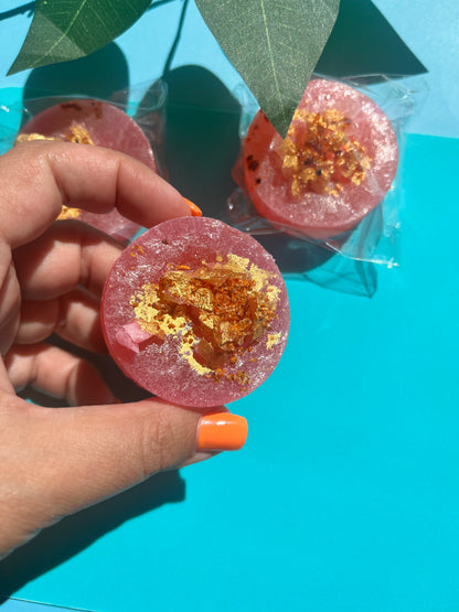 Pink candy with gold flakes held by a hand against a blue background