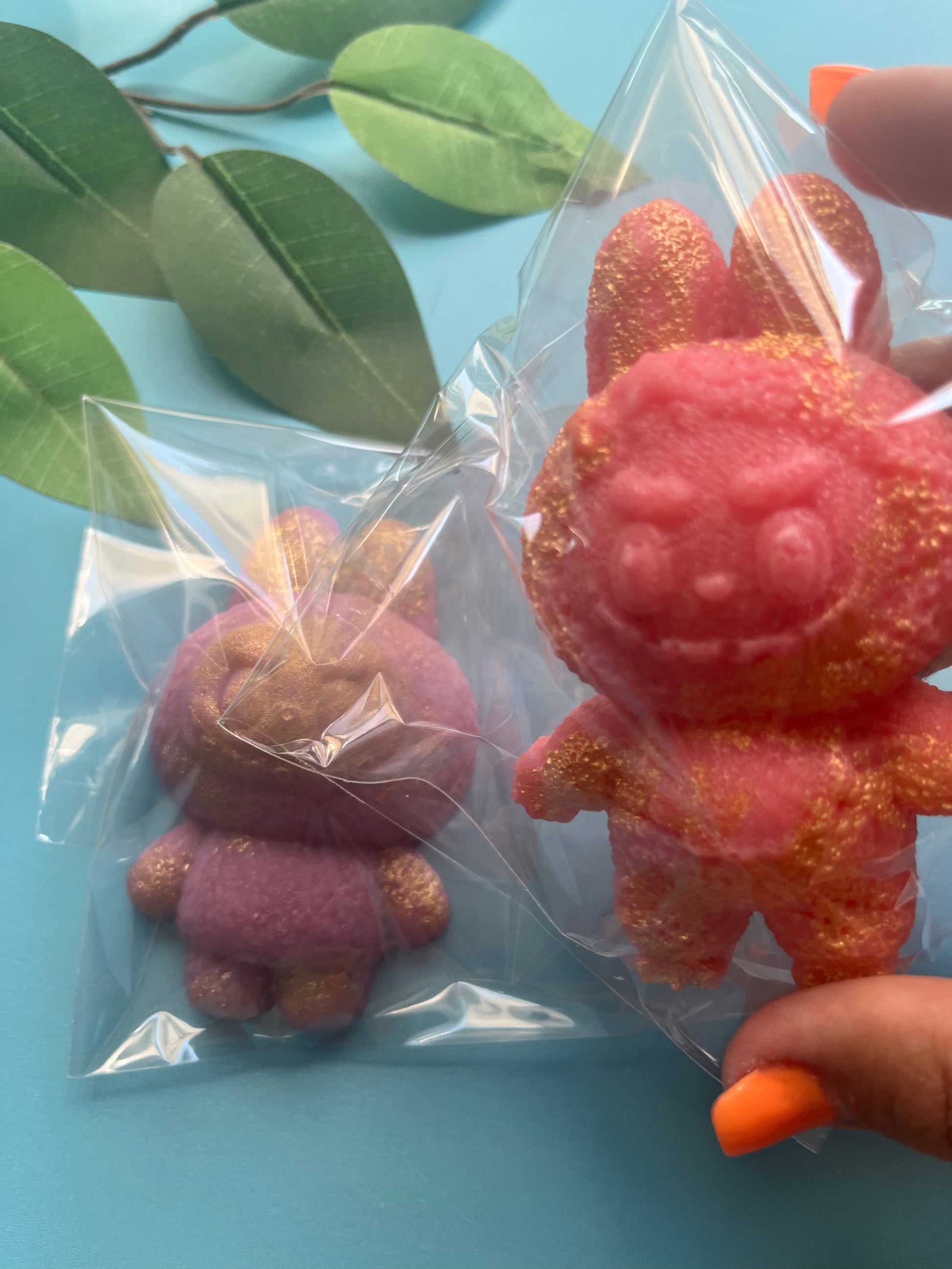 Pink and purple crystal candy monsters in clear packaging on a blue surface with green leaves.