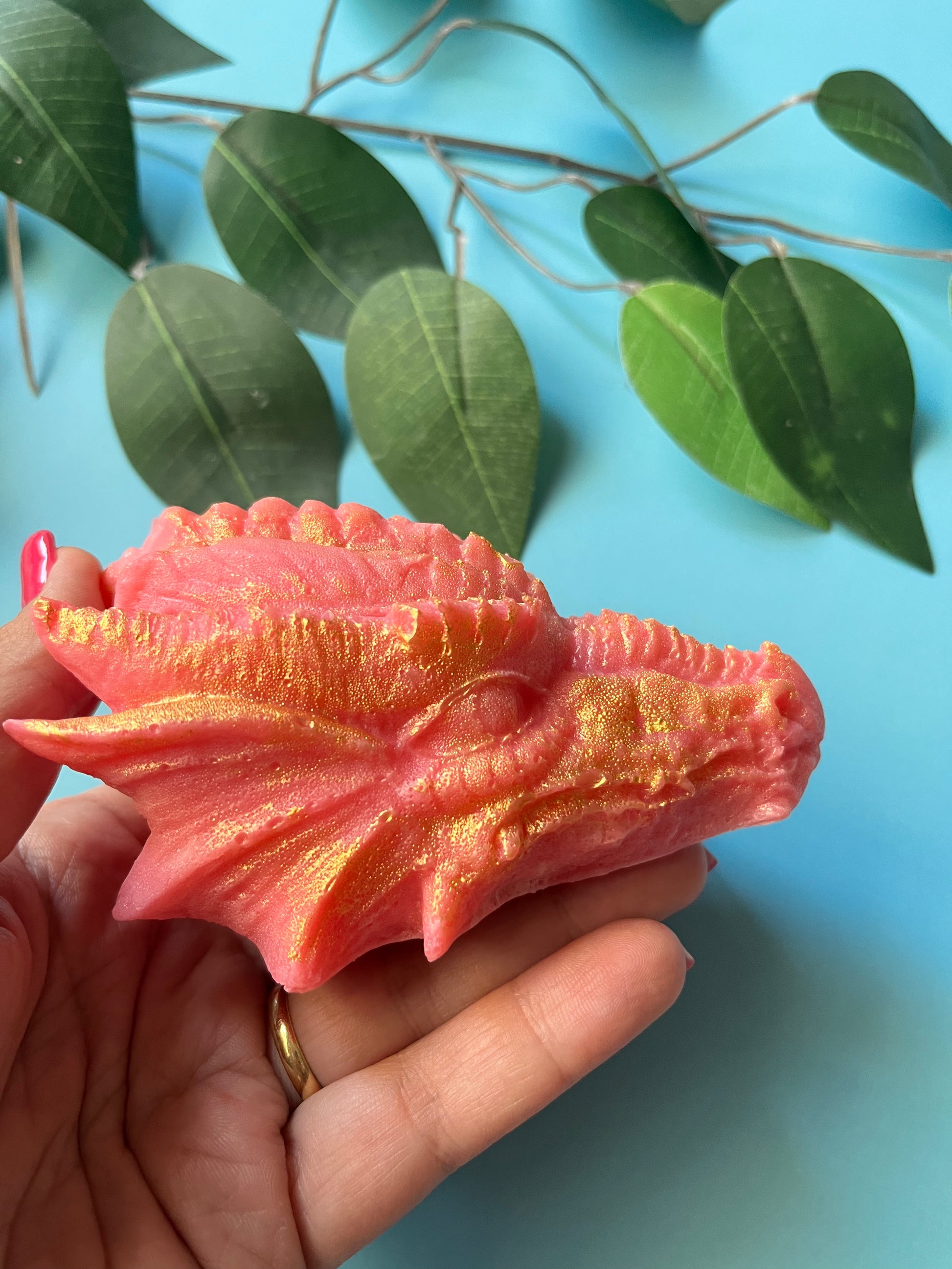 Close-up of an XL dragon head candy in pink with gold shimmer detailing, resting in a person’s hand