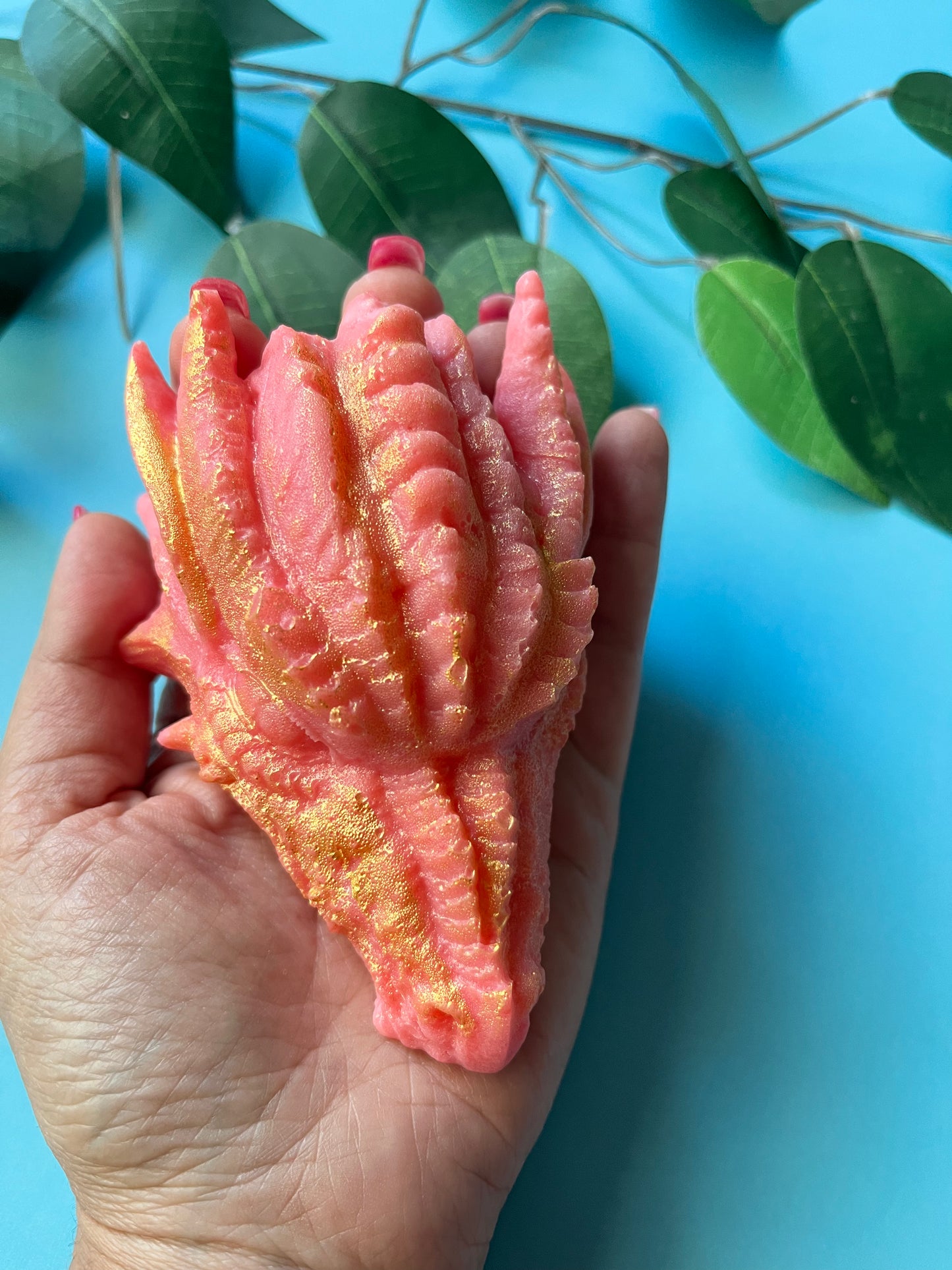 Fantasy-themed dragon head confection, pink with metallic gold highlights, photographed with leafy backdrop
