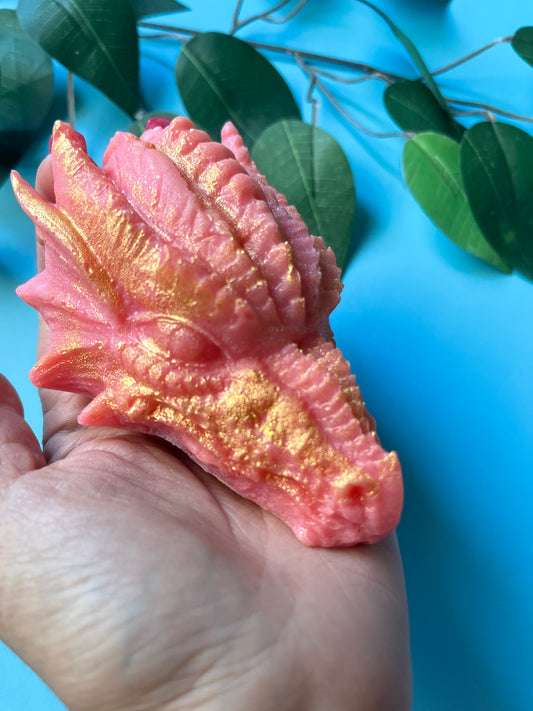 Hand holding a large pink and gold shimmering dragon head crystal candy against a blue background with green leaves